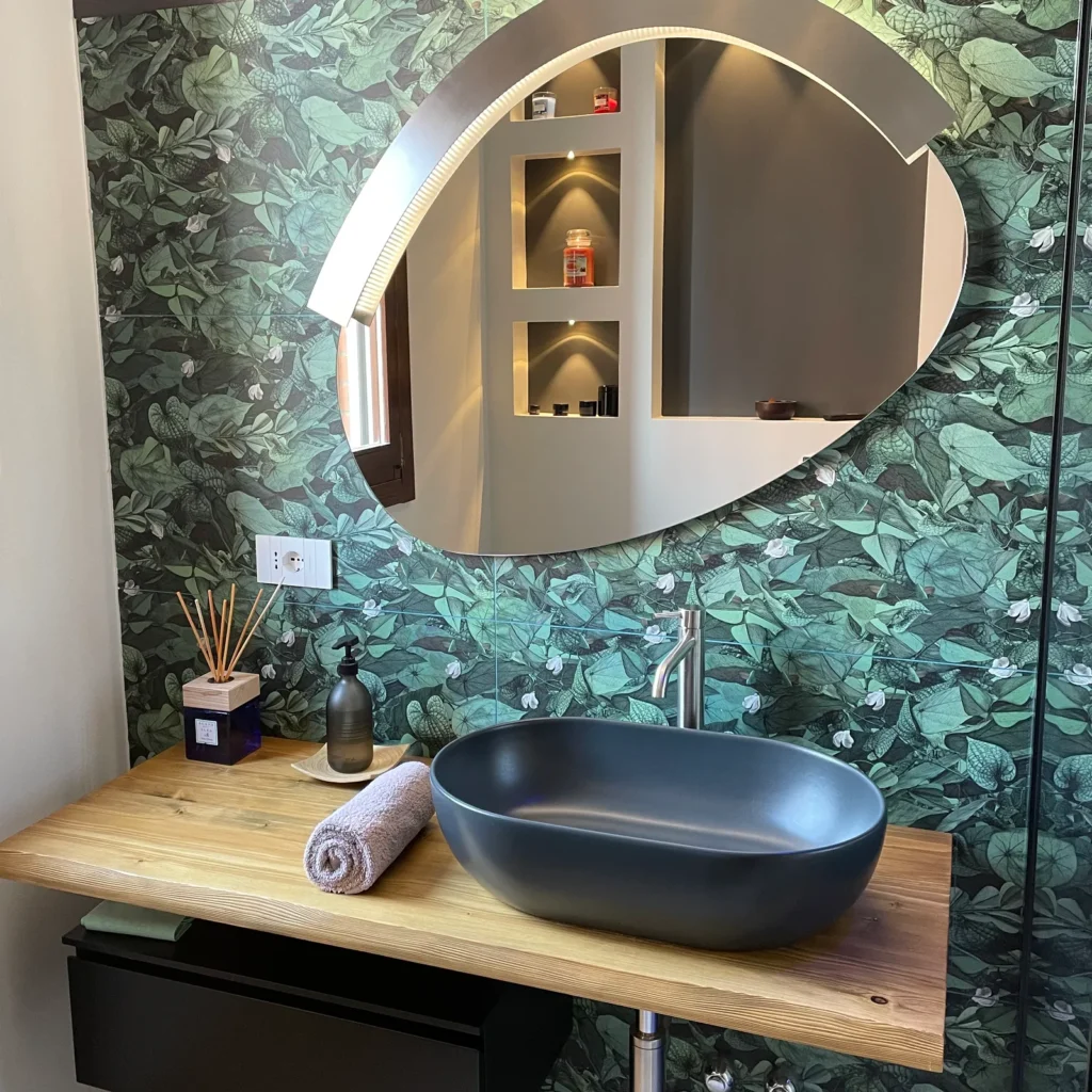lavabo da appoggio su un moderno piano in legno naturale, una parete rivestita in ceramica dai motivi floreali