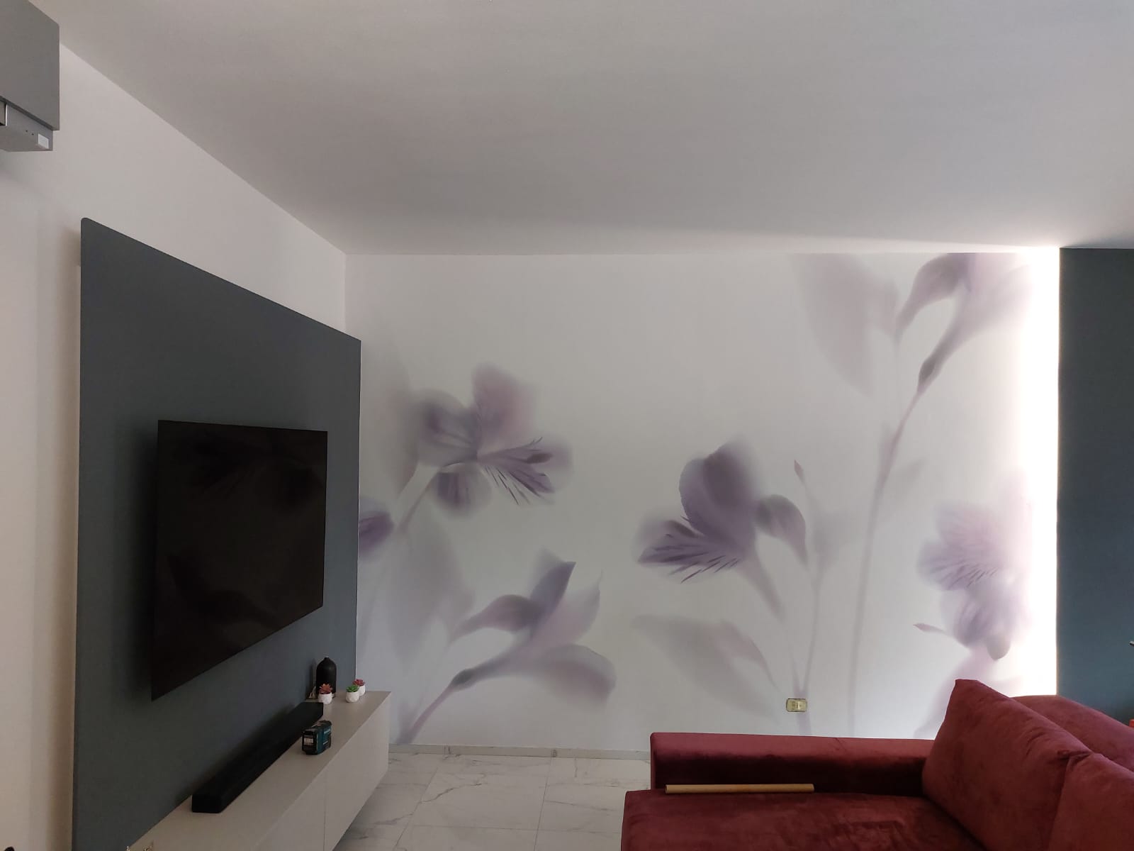 parete con carta da parati floreale ed una grande tv a schermo piatto di fronte a un divano